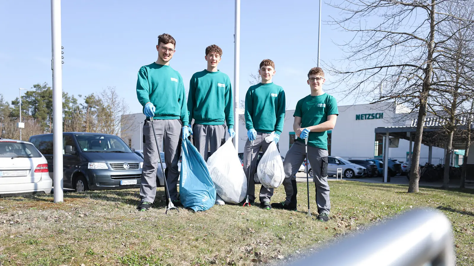 Four NETZSCH apprentices in green shirts and gray pants holding trash bags and litter pickers during a community cleanup event.