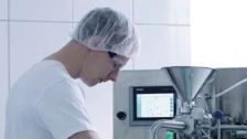 A technician in a hairnet and goggles operates equipment in a clean pharmaceutical facility, focusing on micronization processes.