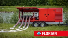 Red mobile rotary lobe pump trailer with multiple hoses, positioned near a body of water, for disaster control at FLORIAN fair.