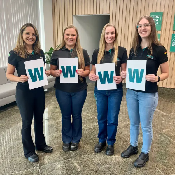 Four female colleagues from NETZSCH Moagem & Dispersão in Brazil hold up signs with the letter "W," celebrating International Women’s Day.