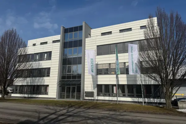 Modern NETZSCH Lohnmahltechnik GmbH office building in Bobingen with clear blue sky and company flags outside.